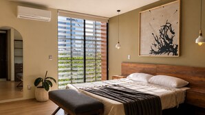 Ein Schlafzimmer mit Bett, Bank, Nachttisch, Kunstwerk und Blick durch ein Fenster.
