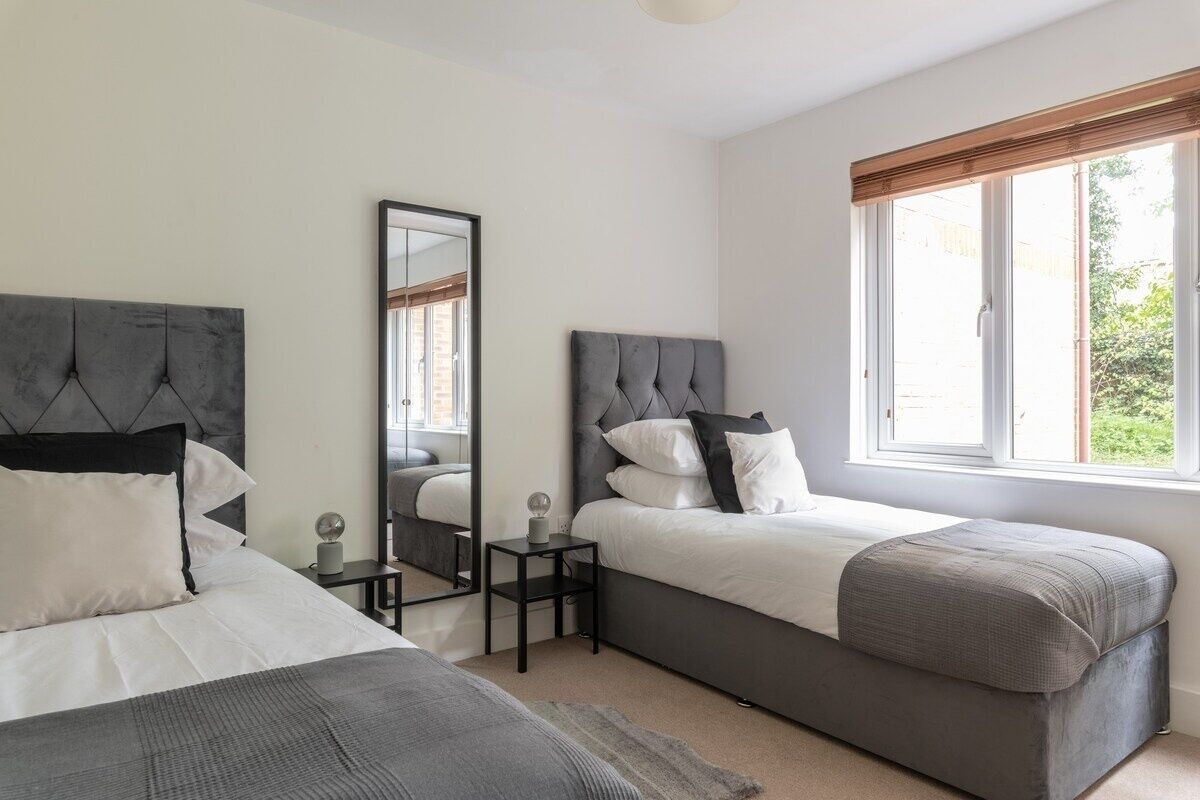 A bedroom with two beds, a large window with a view, and a mirror.