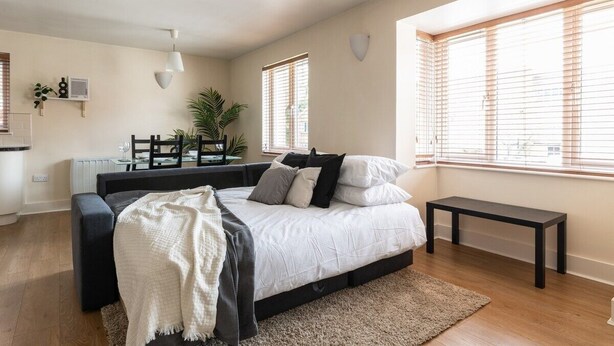 Een slaapkamer met een bed, nachtkastjes, een bankje, een radiator, een raam met zonwering en een plant.
