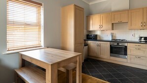 Eine Küche mit Holzschränken, einem schwarzen Fliesenboden und einem Fenster mit Jalousien.