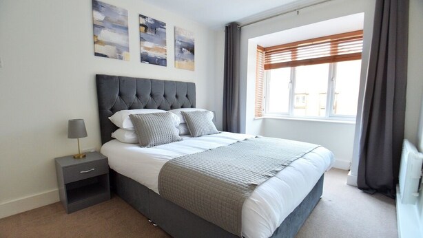 Une chambre à coucher moderne avec un grand lit, une table de chevet, une lampe et des œuvres d’art accrochées au mur.