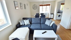 Un salon moderne avec un canapé d’angle gris foncé, une table basse blanche et une grande fenêtre.