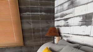 A bed with grey bedding and decorative pillows, a lamp on a bedside table, and a wooden wall with a distressed finish. - Tiny House on Walnut Grove (Ashland)