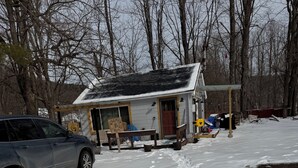 A snow-covered ground with footprints leading to a house with a solar panel roof. - Tiny House on Walnut Grove (Ashland)
