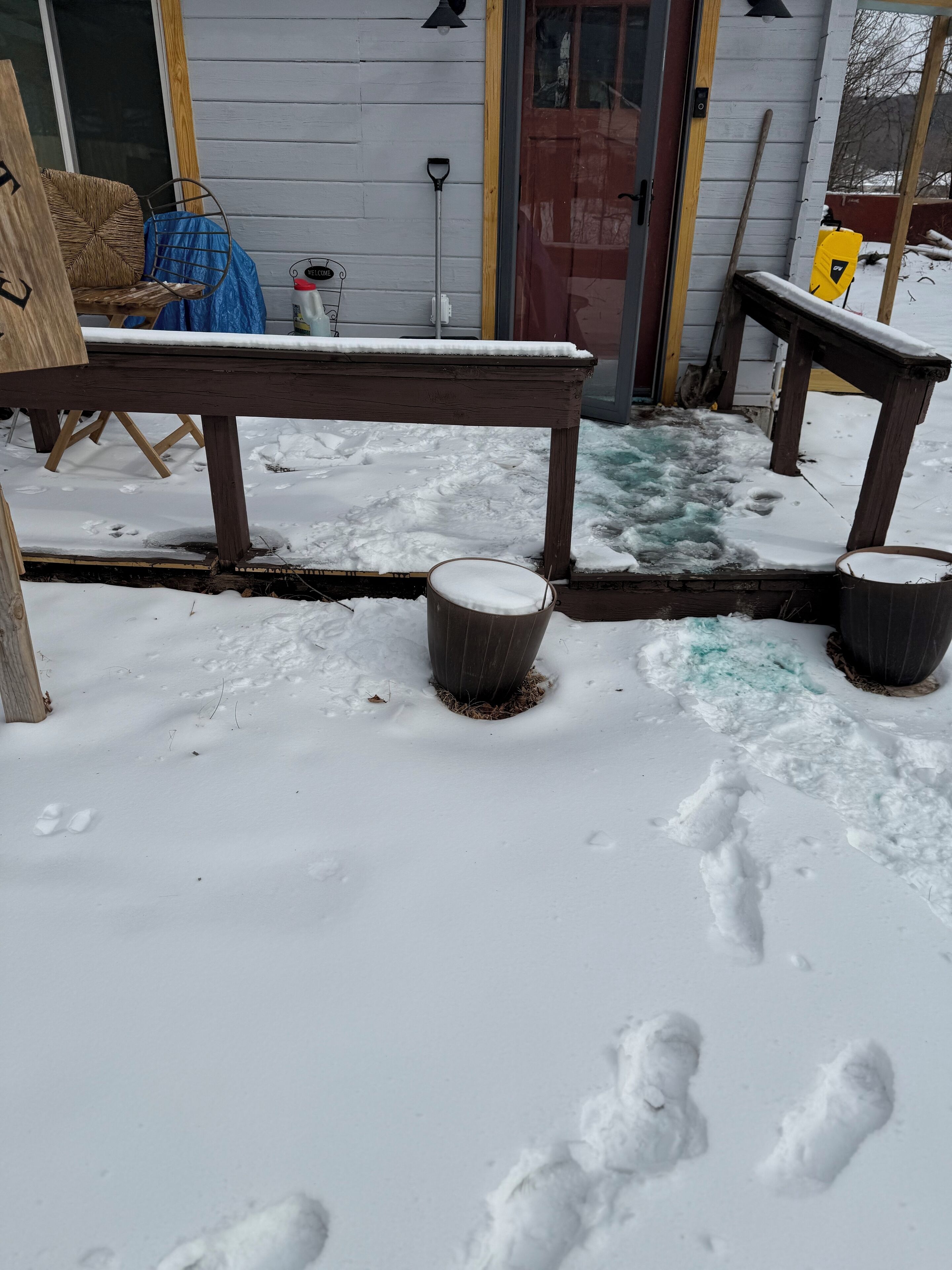 Eine hölzerne Bank und zwei Mülleimer in einer verschneiten Außenanlage.