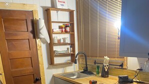 A kitchen with a wooden door, a sink, cabinets, and a Bosch dishwasher. - Tiny House on Walnut Grove (Ashland)