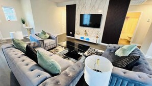 Una sala de estar moderna con un televisor de pantalla plana grande, sofás capitonados, una mesa de centro y un mueble consola decorativo.
