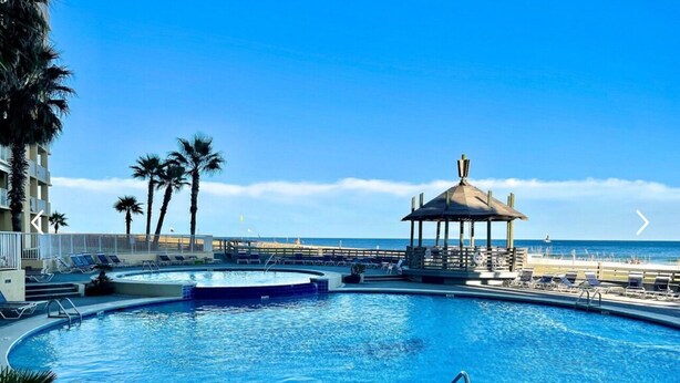 A swimming pool with lounge chairs and a gazebo, overlooking a beach. - Amazing Corner Views, Huge Balcony on the Beach! Newly Remodeled Inside and Out! (Orange Beach)
