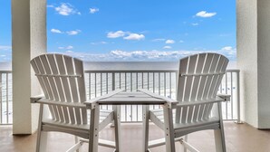 A balcony with two Adirondack chairs and a small table, overlooking a beach with a railing and the ocean. - Amazing Corner Views, Huge Balcony on the Beach! Newly Remodeled Inside and Out! (Orange Beach)