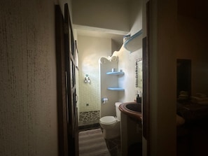 A narrow hallway leading to a bathroom with a toilet, sink, and towel rack.