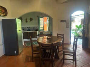 Una cucina con frigorifero, un tavolo da pranzo con sedie, un pavimento piastrellato e un'apertura che dà su uno spazio esterno.