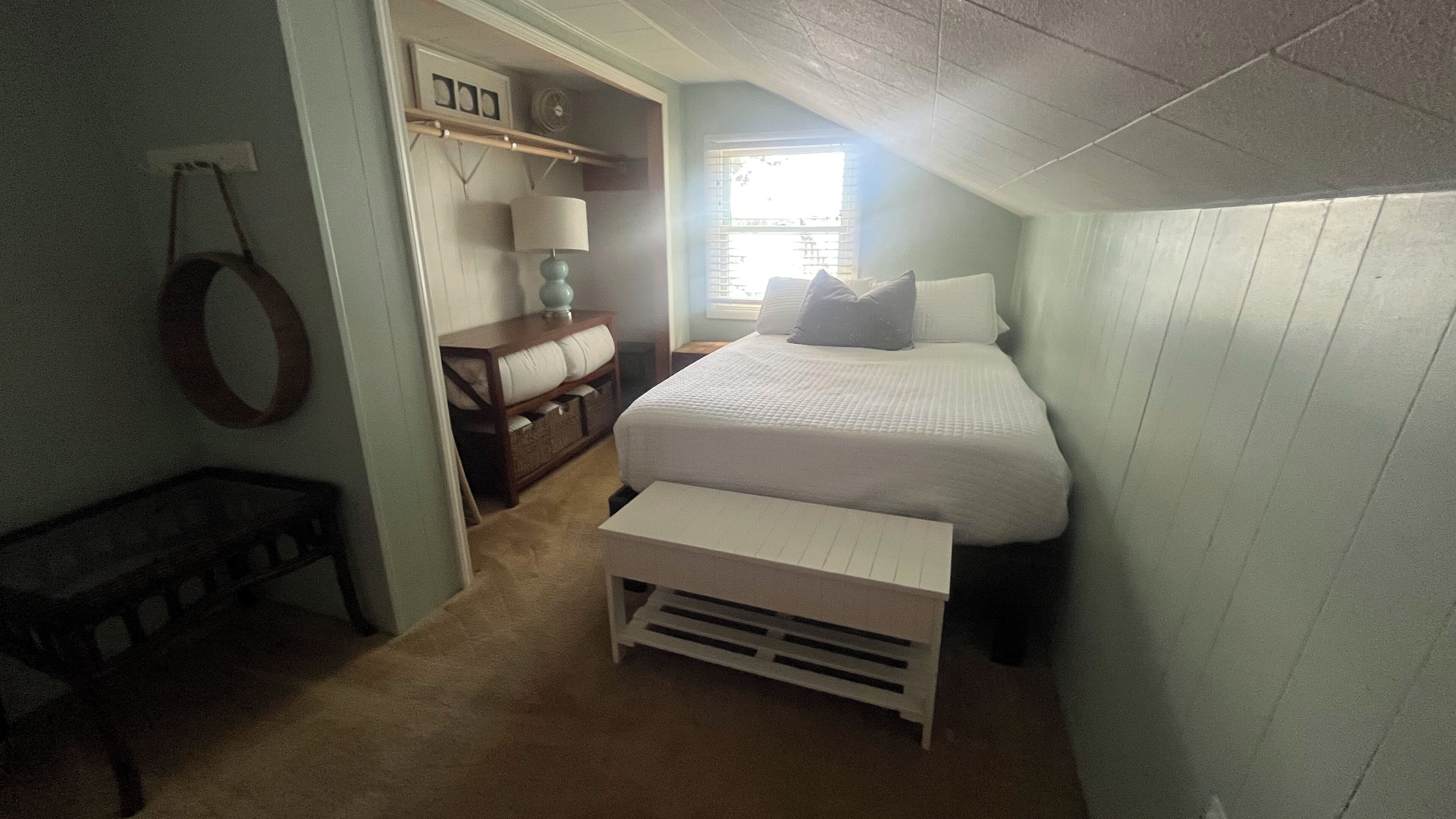 Un dormitorio con cama, mesita de noche, lámpara y una pequeña banca.