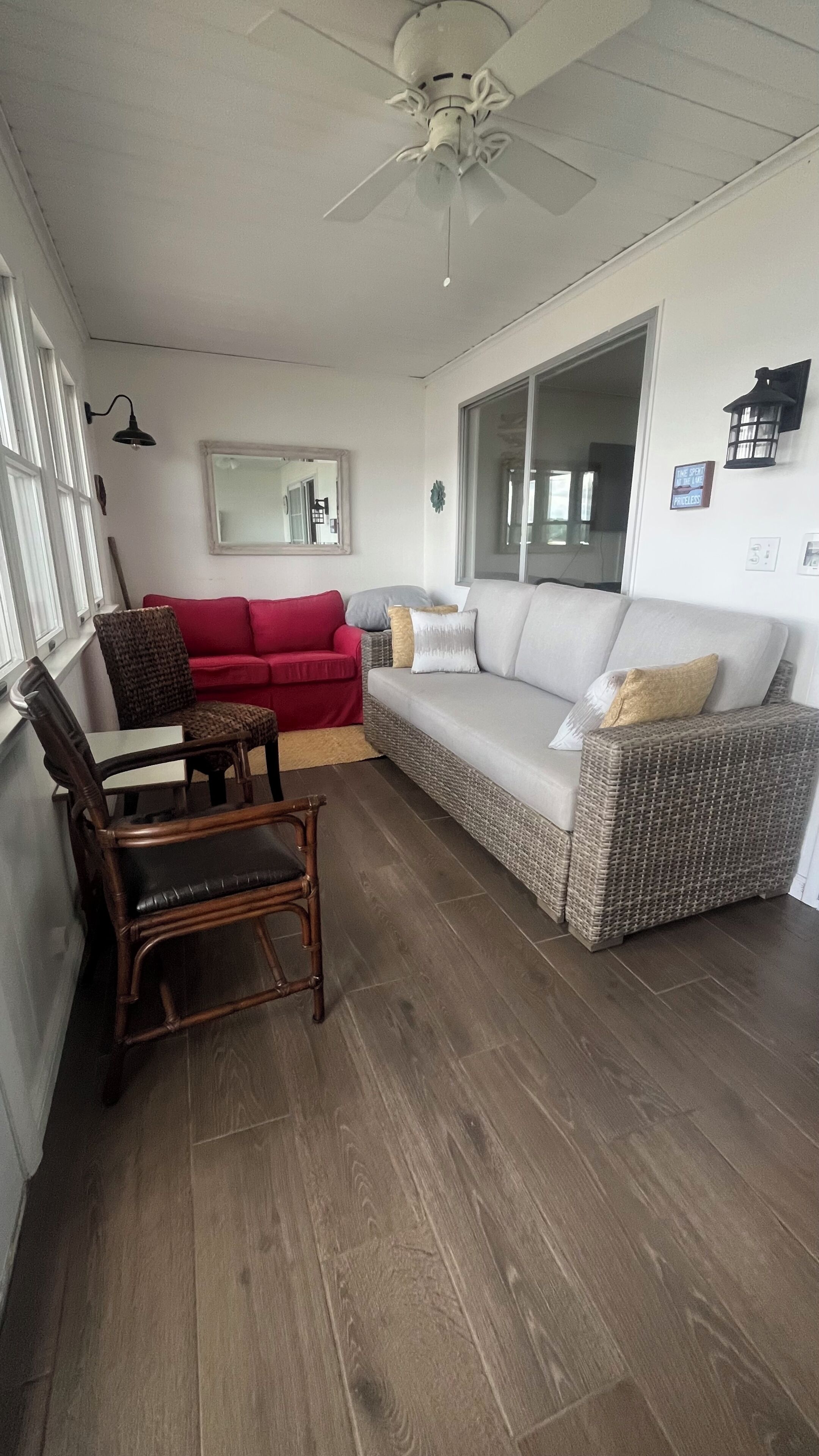 Ein Wohnzimmer mit einem roten Sofa, einem weißen Sofa, einem Holzstuhl, einem Deckenventilator und einem großen Fenster.