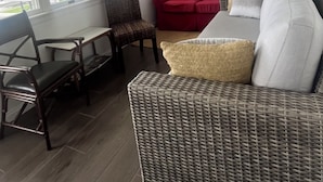 Una habitación con ventilador de techo, un sofá rojo, un sofá de mimbre, una mesa de comedor con sillas y ventanas grandes.