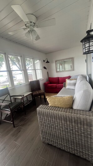 A room with a ceiling fan, a red sofa, a wicker sofa, a dining table with chairs, and large windows.