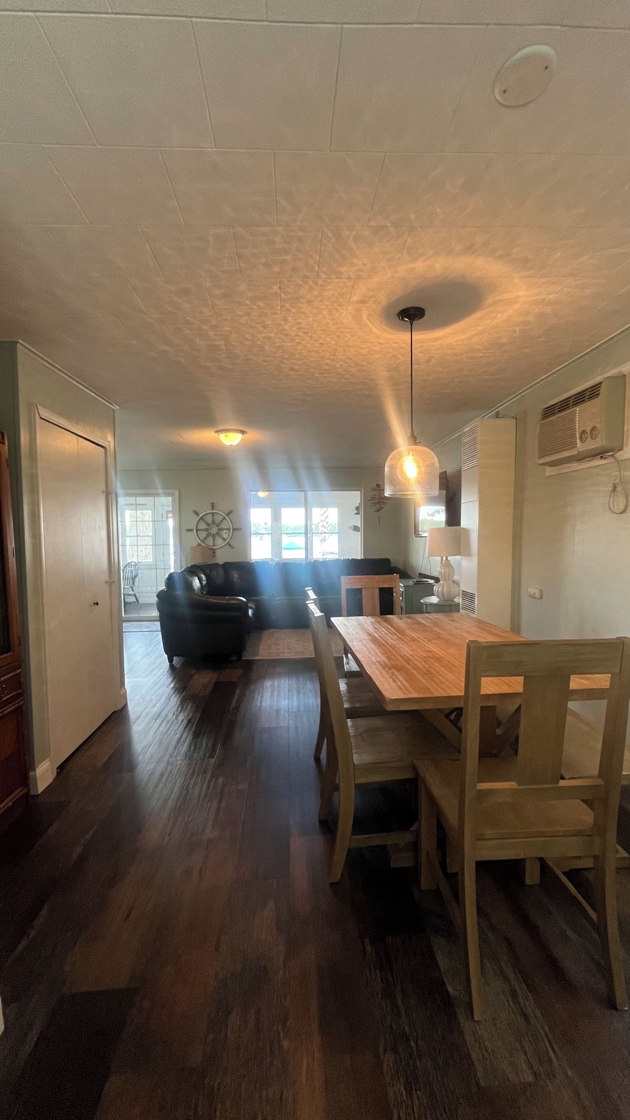 A dining area with a wooden table and chairs, a pendant light, and a view of the living room in the background.