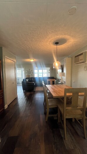 Un comedor con una mesa y sillas de madera, una lámpara colgante y vista al salón.