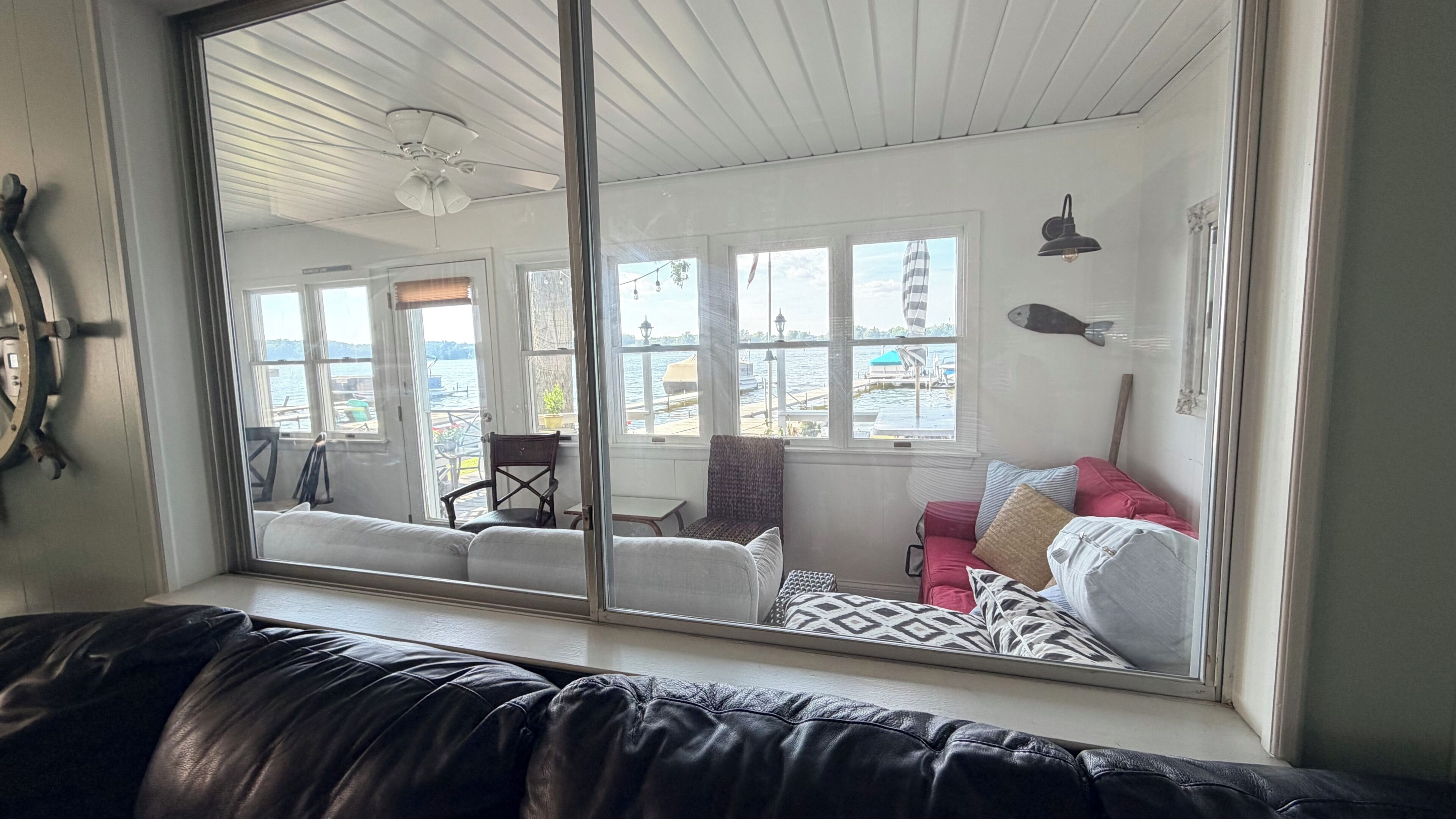 Una habitación con un ventanal grande, ventilador de techo, sofá rojo y vista al agua.