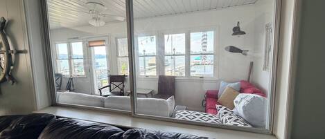 Ein Zimmer mit großem Fenster, Deckenventilator, rotem Sofa und Blick auf das Wasser.