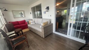 En stue med en rød sofa, en fletsofa, en træstol og en glasdør, der fører til et spiseområde.