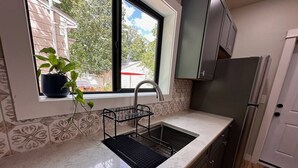 Une cuisine avec un évier, une fenêtre ornée d’une plante et un réfrigérateur.