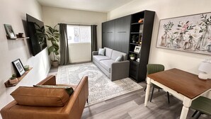 Un salon moderne avec un canapé gris, une table basse en bois, une table à manger avec des chaises et une grande fenêtre avec des rideaux.
