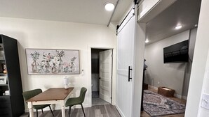 Un coin repas avec une table et des chaises en bois, un tableau accroché au mur et une porte coulissante donnant sur une autre pièce.