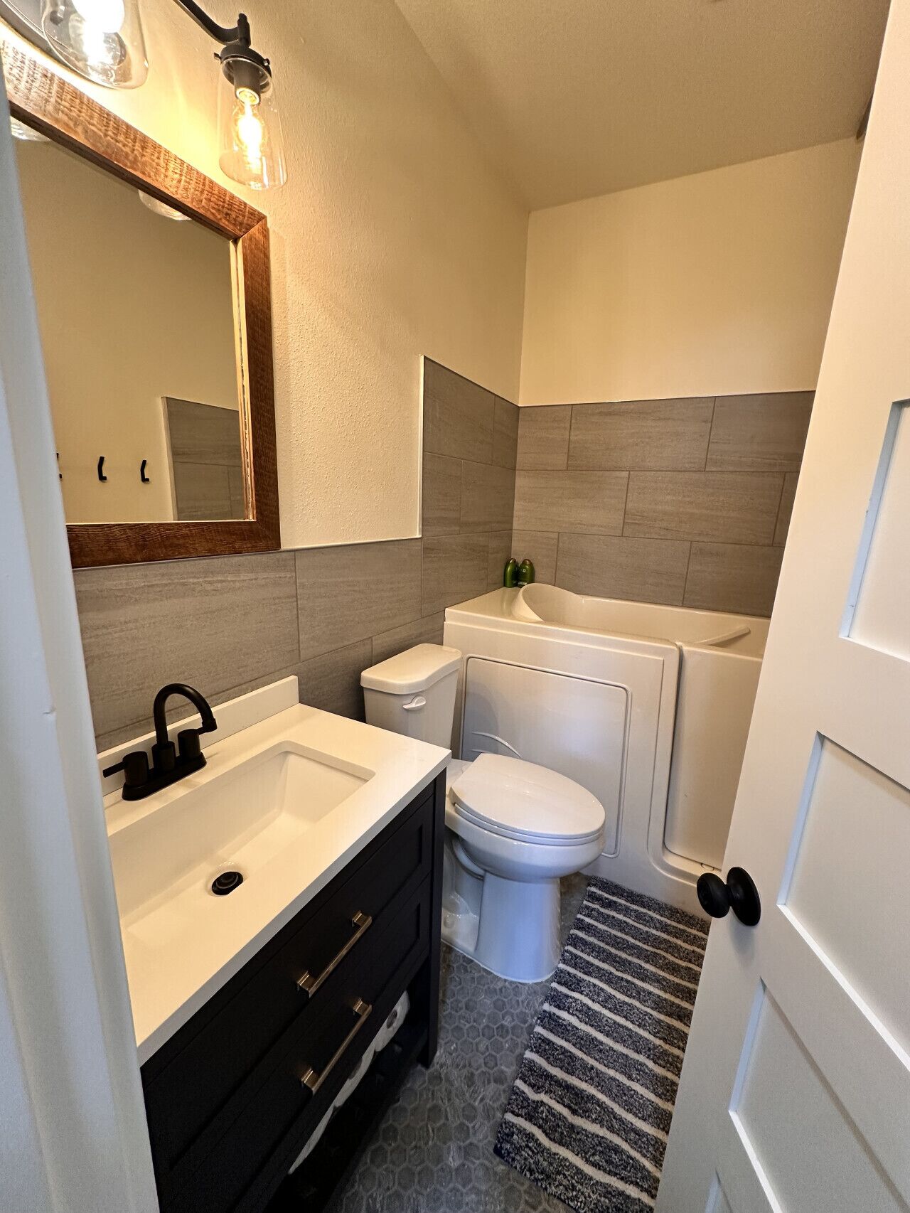 Un baño moderno con un lavamanos blanco, tocador negro, inodoro y bañera.