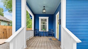 Een blauwe veranda met een houten vloer, witte leuningen en twee stoelen.