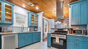 Een keuken met turquoise kastjes, roestvrijstalen apparatuur en een houten plafond.
