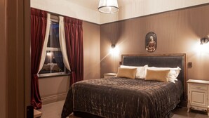 Un dormitorio con una cama grande, una mesita de noche, una lámpara de pared y una ventana con cortinas.