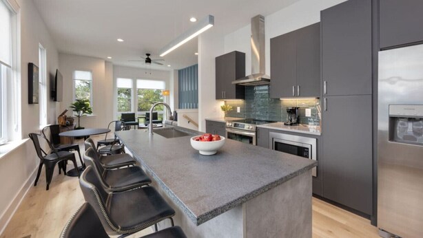 A modern kitchen with a central island, dark cabinetry, and a stainless steel refrigerator. - `The Ryman` 4BR Haven with Scenic Rooftop (Nashville)