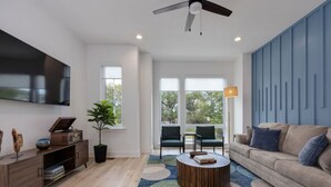 A modern living room with a large flat-screen TV, a wooden coffee table, a beige sofa, and a blue accent wall. - `The Ryman` 4BR Haven with Scenic Rooftop (Nashville)