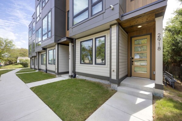 A modern two-story residential building with a front entrance, a visible mailbox, and a well-maintained lawn.