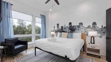 Quarto moderno com uma cama grande, um sofá de couro preto, uma obra de arte com paisagem urbana e vista para a cidade pela janela.