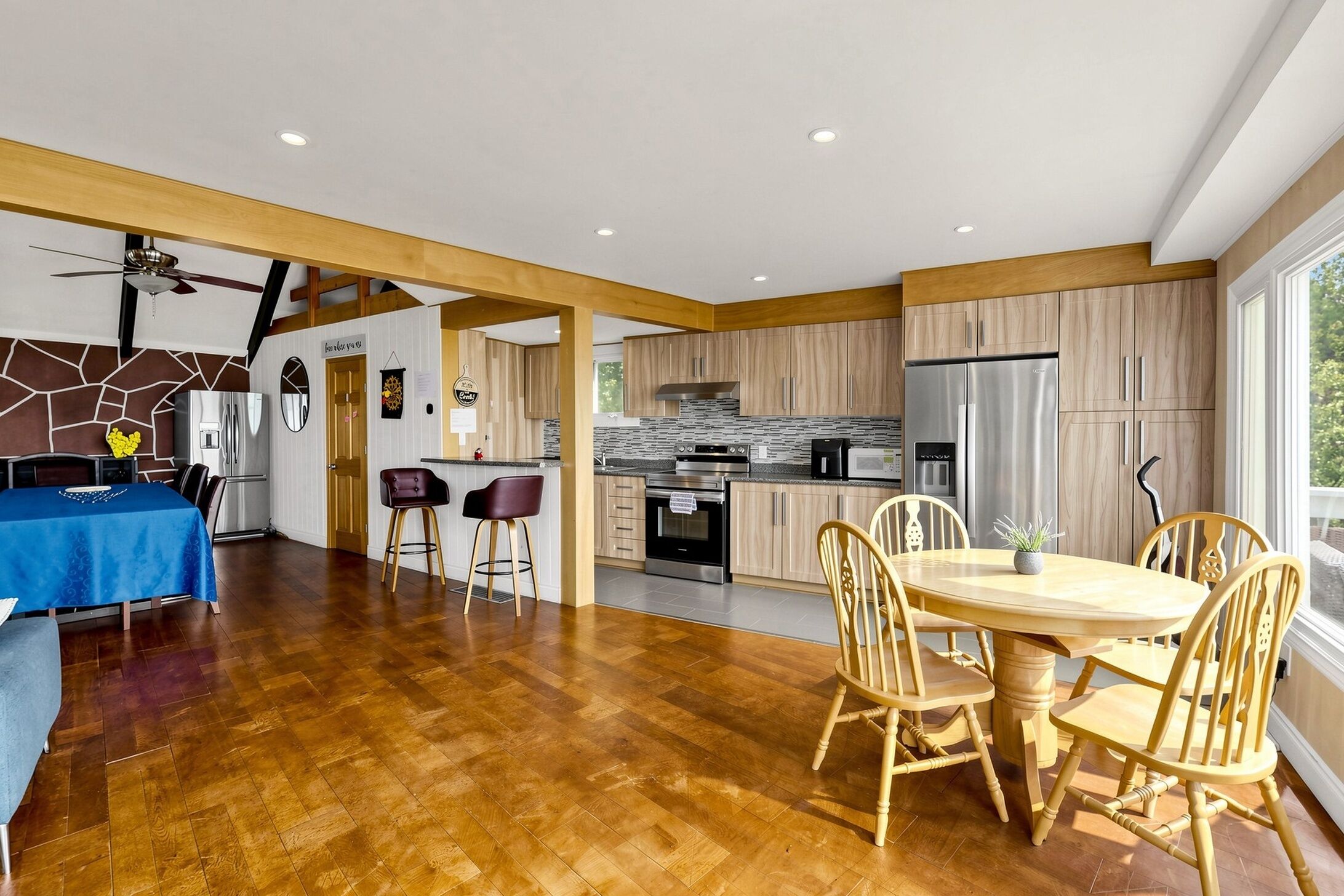 Eine moderne Küche mit Holzschränken, einem Edelstahlkühlschrank und einem Essbereich mit rundem Tisch und Stühlen.