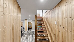 Eine Holztreppe in einem Flur mit grauem Holzboden, die zu einem Zimmer mit einem Bett und einem Schreibtisch führt.