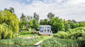 Ein Haus am Seeufer mit einer Anlegestelle, umgeben von üppiger Vegetation und Bäumen.