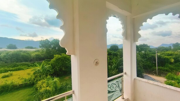 Un balcon offrant une vue sur un paysage verdoyant et luxuriant, avec des montagnes à l’horizon.