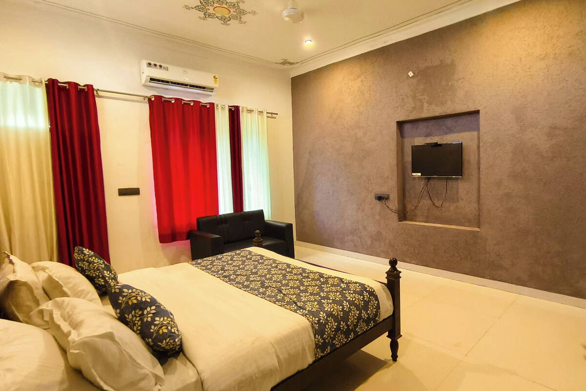 Un dormitorio con cama, sofá, televisor montado en la pared y aire acondicionado.