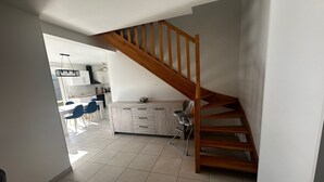 A modern kitchen with a wooden staircase, a dining area with blue chairs, and a kitchen island.