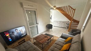 A living room with a sofa, a coffee table, and a TV displaying a show. There is a staircase leading to another room.