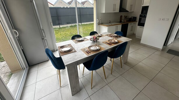 A modern kitchen with a dining table set for four, white cabinets, and a large window overlooking a backyard.