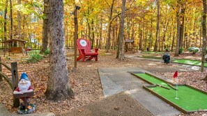 Un camping con mesas de picnic, una silla roja, un campo de mini golf y una estatua de gnomo.