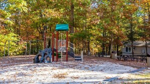 Une aire de jeux avec une structure d’escalade et des toboggans, entourée d’arbres et comprenant un espace pique-nique.