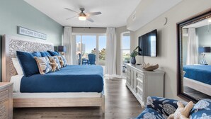 A bedroom with a large bed, a ceiling fan, a TV, and a view of the balcony. - Emerald Escape! Newly remodeled spacious 3-bedroom condo with oversized balcony! (Destin)