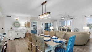 A dining area with wicker chairs, a wooden table set for four, and a ceiling fan. - Emerald Escape! Newly remodeled spacious 3-bedroom condo with oversized balcony! (Destin)