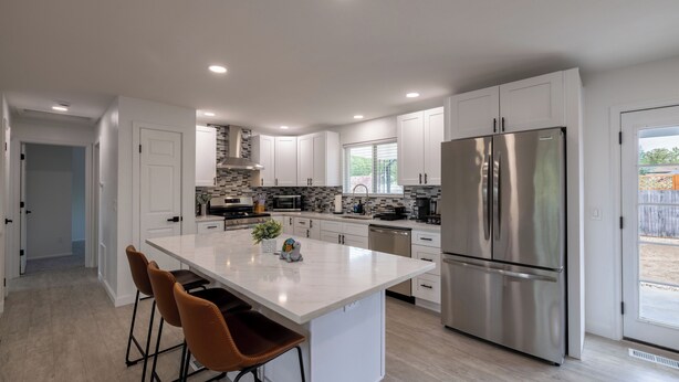 A modern kitchen with white cabinetry, a large stainless steel refrigerator, and a central island with bar stools. - 5BD I Game Room I Backyard & BBQ I 20 Mins to DEN (Thornton)