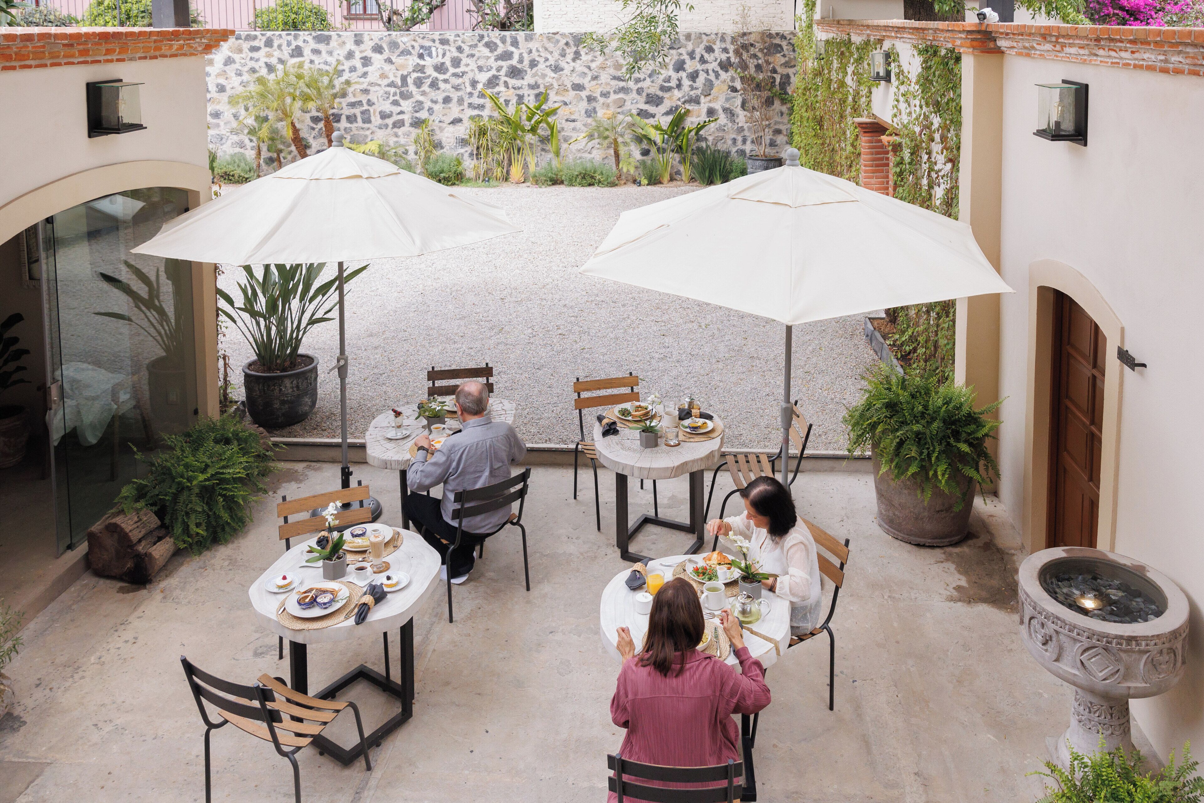 A patio area with tables and chairs, surrounded by potted plants and a stone wall.