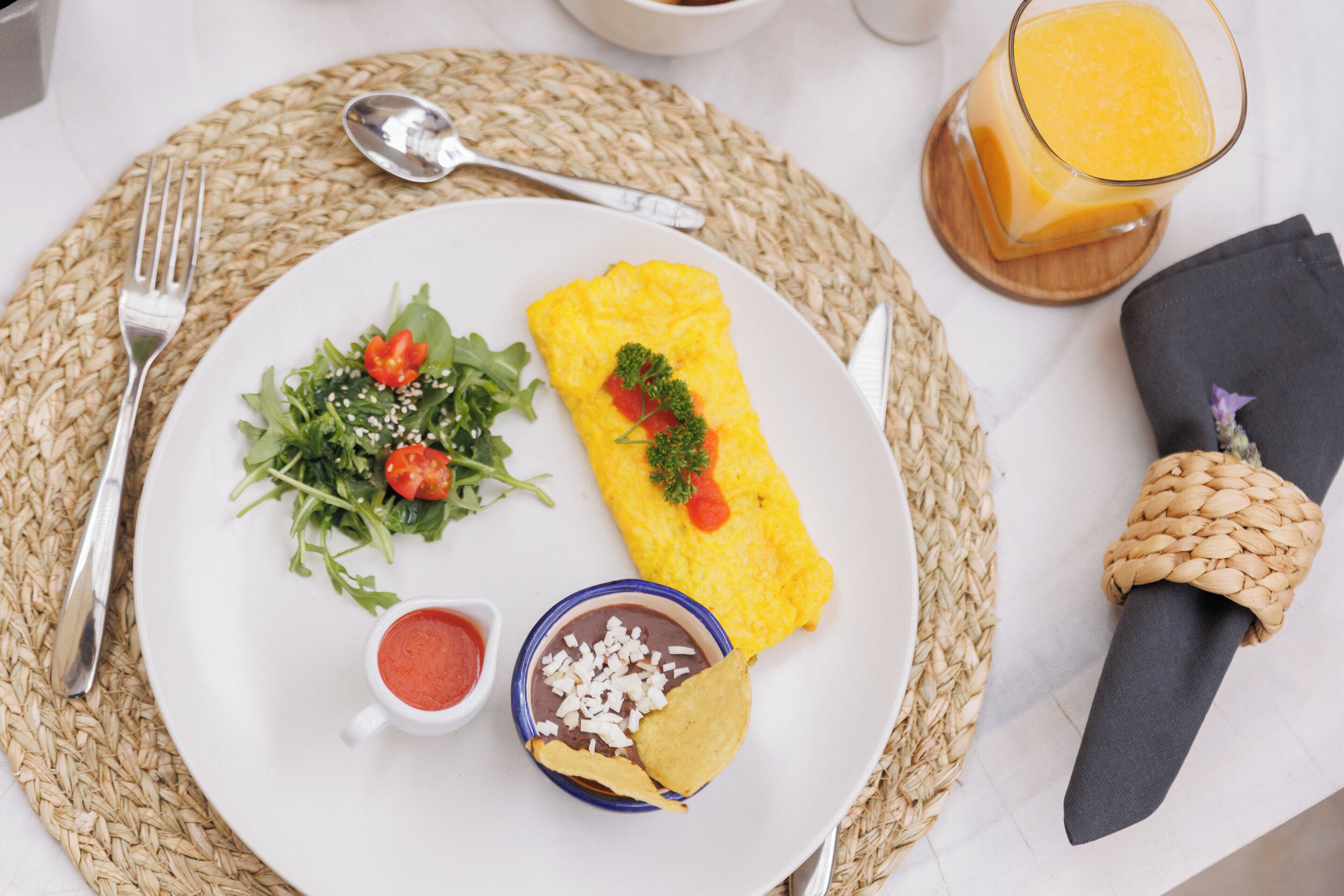 A plate with a rolled omelette, a salad, and a bowl of beans with chips.
